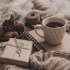 Sweaters and cup of tea with notebook, candle and knitting clothes. Cozy autumn or winter concept.