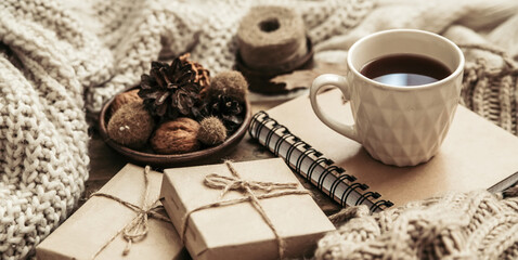 Sweaters and cup of tea with notebook, candle and knitting clothes. Cozy autumn or winter concept.