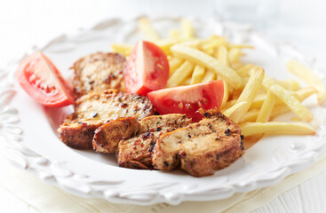 Fried pork tenderloin with french fries and tomatoes. Close up.