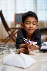 Asian Schoolboy playing with toy aeroplane while doing homework