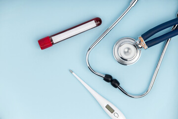 Stethoscope with thermometer and tube of blood test on blue background.