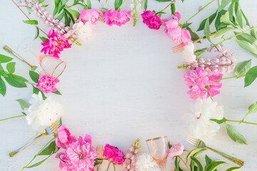 Obraz na płótnie Canvas Floral background with pink, white, purple peonies, wineglasses and golden forks on white paint wooden background. Frame of peones. Space for text