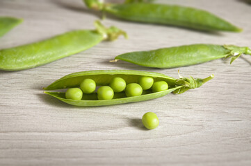 Green pea grains are scattered on a rustic style. Opened pea pod on table background. Selective focus.
