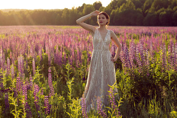 A girl in an evening dress on the field of lupins. A girl in a beautiful dress on a field among purple flowers.