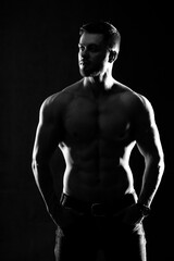Fototapeta na wymiar Strong athletic man fitness model. Male showing six pack abs. Isolated on dark background. Black and white photo.