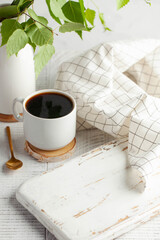A white mug with black coffee, a branch with green leaves, an empty Board, a place to insert your product. Copy space