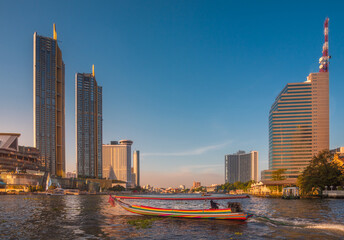 Skyscrapers and Traditional Long Tail Speedboat on the Chao Phraya River in Bangkok, Thailand during Golden Hour