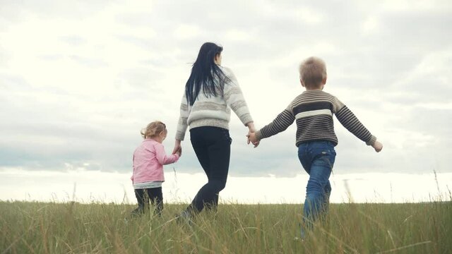 happy family. mom and little children walk in the park teamwork outdoors holding hands. woman and little boy and girl walk lifestyle on a green field at sunset