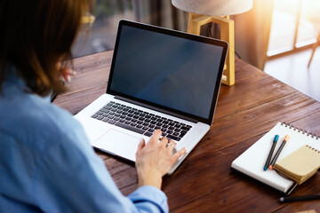 Mockup image of a woman using laptop with blank screen on wooden table