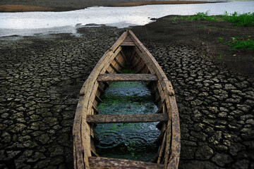 Old canoe on dry lake, river on background,  clay cracked soil, mud ground. Climate change,...