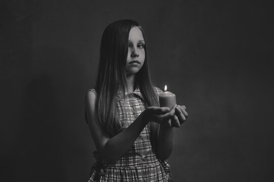 girl holding a candle in her hands with a sad face