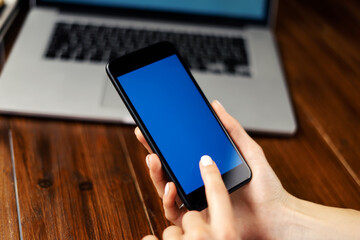 Mockup image of a woman using smartphone with blank screen on wooden table. Close up photo of female hands holding mobile phone vertically