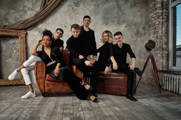 multi ethnic jazz band posing on a leather sofa against the gray wall in loft. Bass guitar player,...