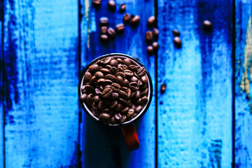 orange cup full of roasted coffee beans on blue wooden table