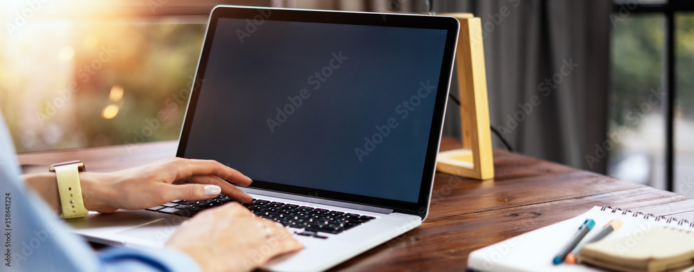 Wall mural mockup image of a woman using laptop with blank screen on wooden table