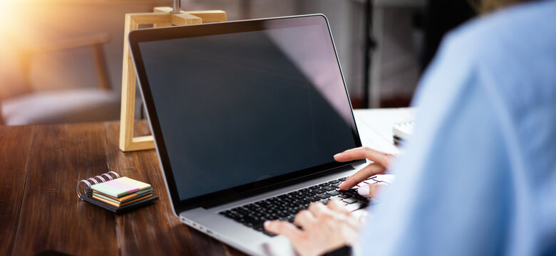 Mockup image of a woman using laptop with blank screen on wooden table