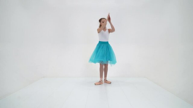 Cute little girl in a tutu and pointe shoes dancing in the studio on a white background.