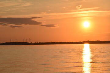 Wind turbines in the Eckernfoerde Bay, in Northern Germany. The setting sun paint the sky and the water of the Baltic Sea with shades of orange and gold.