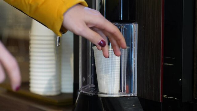 Woman place empty paper cut into coffee machine and close small door, close up shot. Customer use coin-operated hot drink vending machine at public place
