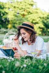 Young beautiful european brunette girl is reading a book in nature. Spends the weekend outside the city, outdoors, a picnic in the park in the meadow. Tasty food, relaxation. Summer time