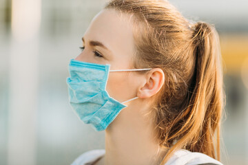 young woman in a medical protective mask stands in the open air. Quarantine, coronavirus