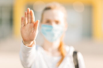 young woman in a medical protective mask stands in the open air and makes a stop gesture. Quarantine, coronavirus