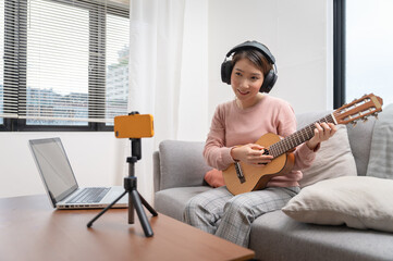 Asian woman blogger recording and live steam playing guitar on social media. Concept of guitarist online lesson while staying at home