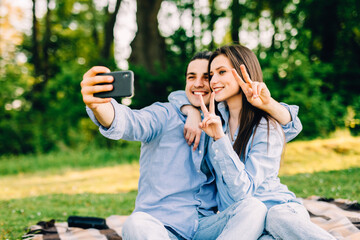 Young loving couple lie on a plaid in the park and use the phone, beautiful guy and girl