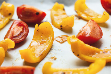 Slices of yellow bell pepper and red tomato prepared for baking with spices, close up