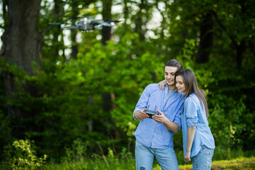 Portrait of man and woman is operating the drone by remote control in the green park. Man and woman is playing with quadrocopter outdoors.