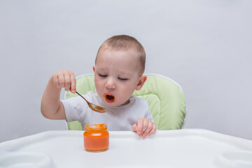 A small boy with an appetite eats a spoonful of mashed carrots in a high chair on a white background