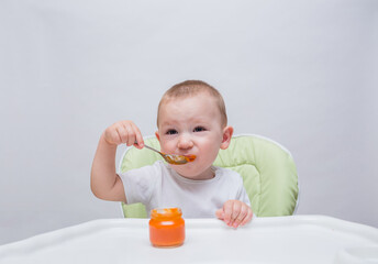 A small boy grimaces at a spoonful of mashed carrots at a table on a white background