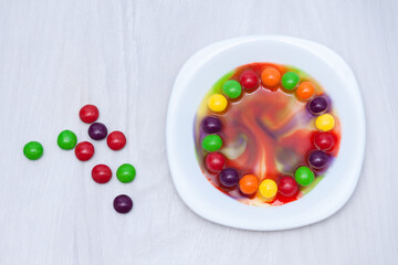 Naklejka na ściany i meble Science experiment for kids. Circle of colored candies on white plate.