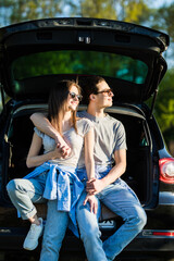 Happy young couple sitting in trunk of their new car in countryside