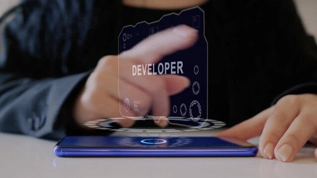 Female hand interacts HUD hologram with text Developer. Woman in black uses conceptual holographic technology of the future on the screen of a smartphone lying on a table