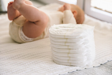 A baby in a diaper at the age of two months and a stack of diapers. How to choose baby diapers - obrazy, fototapety, plakaty