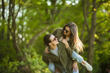 Young man giving his pretty girlfriend a piggy back in the park smiling at camera on a sunny day