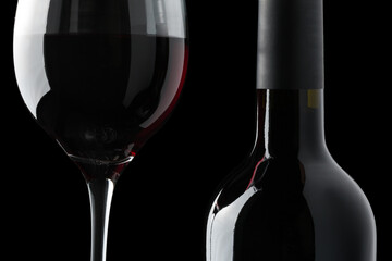 Detail of a glass of red wine next to a bottle on a black background