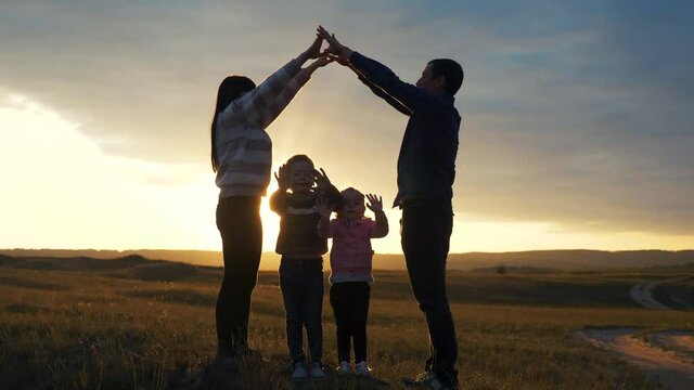 happy family. teamwork adult parents and small children shows a house and comfort symbol silhouette at sunset. happy family mom dad and lifestyle kids children portray a house roof hold their hands