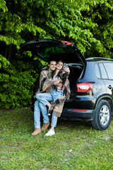 Young people take selfie on phone in car trunk in forest at picnic