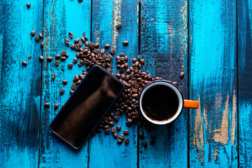 filtered morning coffee in an orange cup and coffee beans with smartphone on blue wooden table