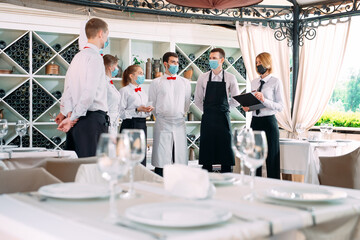 Employees of a Restaurant or Hotel in protective masks. End Of Quarantine. Restaurant Manager and his staff on the terrace. interaction with the chef in the restaurant.