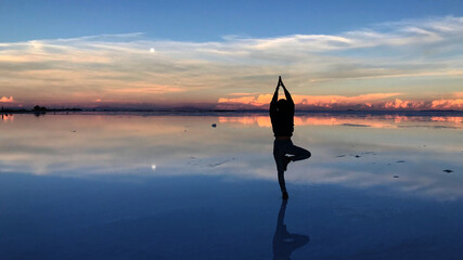 Sunset with lady in yoga pose and water reflection in Salar de Uyuni, Bolivia