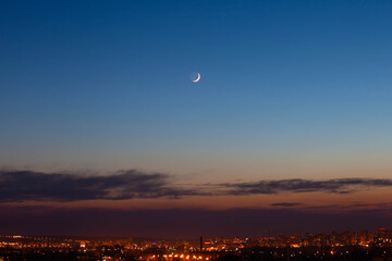A month against the blue sky with stars and the city with evening lights
