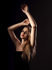 Naklejka premium Attractive make-up blond hair style woman elegant posing and holding arms above. Treatment and soft care about hands skin. Art shadow portrait on black background
