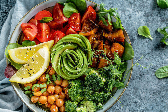 Buddha bowl salad with baked sweet potatoes, chickpeas, broccoli, tomatoes, greens, avocado, pea sprouts on light blue background with napkin. Healthy vegan food, clean eating, dieting, top view