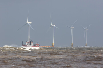 Ship on rough sea horizon by offshore wind farm turbines.