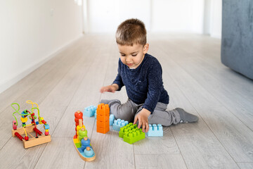 Small boy three or four years old playing on the floor at home - Little caucasian child spending free time alone with brick blocks and creative toys - creativity childhood care growing up concept