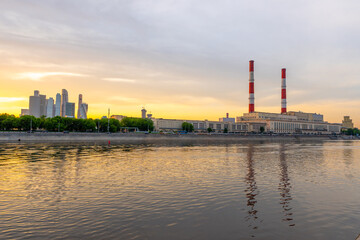 Sunset at Moscow river, amazing reflections on the water. Pipes of a thermal power plant with white and red stripes. 