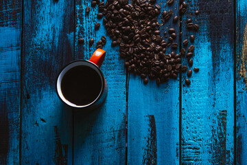 morning coffee in an orange cup with roasted whole coffee beans on blue wooden table